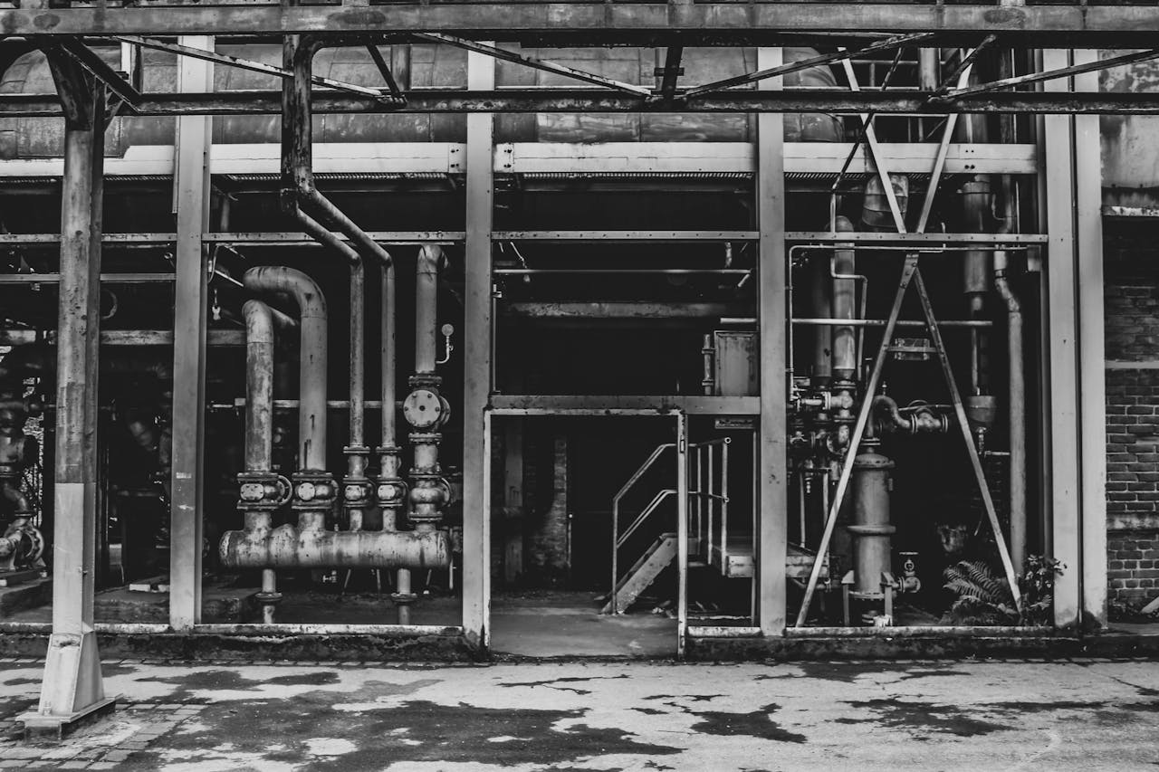 A black and white photo of an abandoned industrial building with exposed pipes and steel structures.